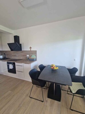 A modern kitchen with a built-in oven, a sink, and a wooden countertop. There is a dining table with four chairs and a bowl of fruit on it. - Holiday apartment with garden and air conditioning (Turanj)