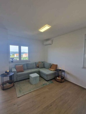 A living room with a sectional sofa, a small table, a round side table, and a window with a view. - Holiday apartment with garden and air conditioning (Turanj)