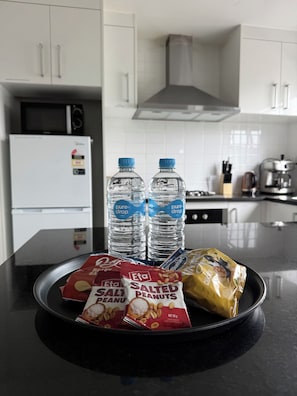 A kitchen counter with a black plate holding water bottles, a bag of salted peanuts, and a bag of chips.