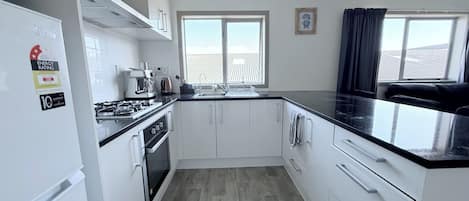 Cocina moderna con armarios blancos, encimera negra y estufa. Se ve una ventana con vista a una valla exterior.