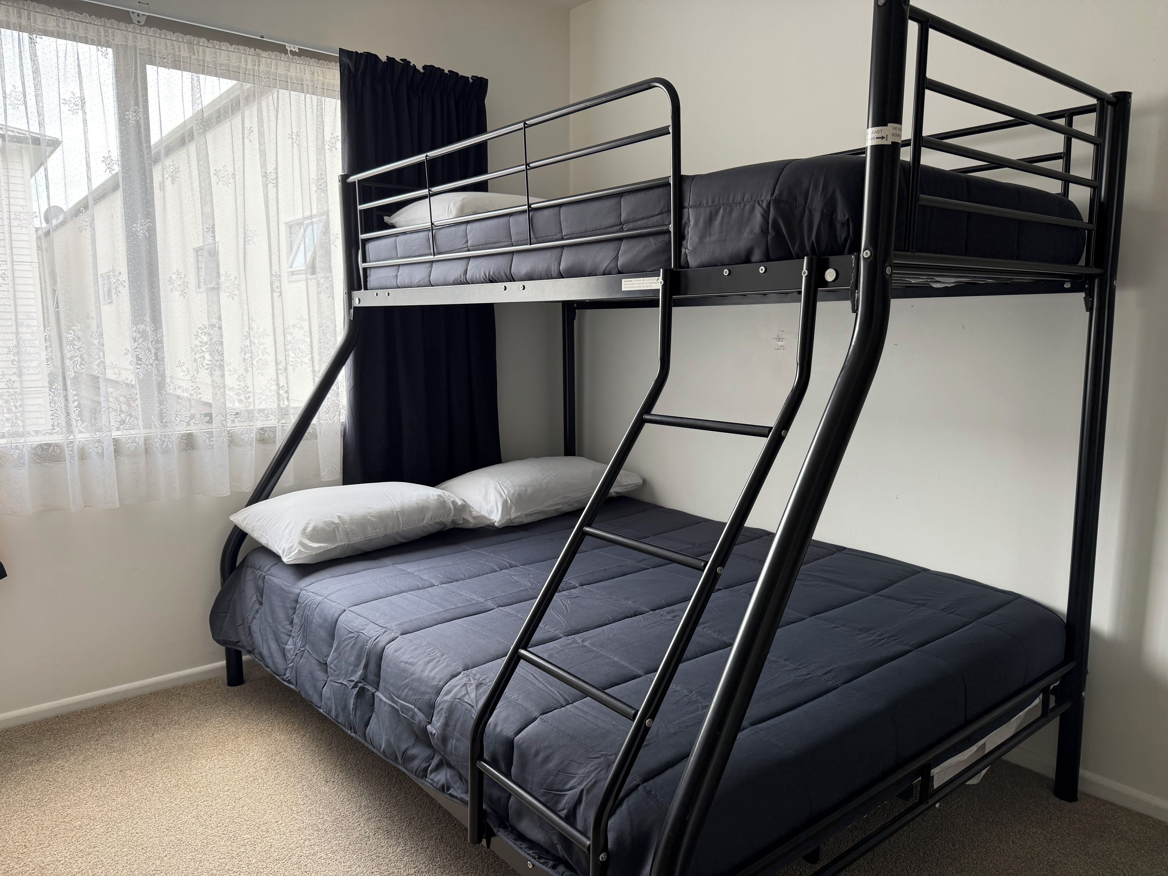 A bunk bed with a mattress and pillows, a window with curtains, and a carpeted floor.