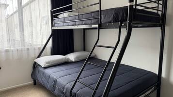 A bunk bed with a mattress and pillows, a window with curtains, and a carpeted floor.