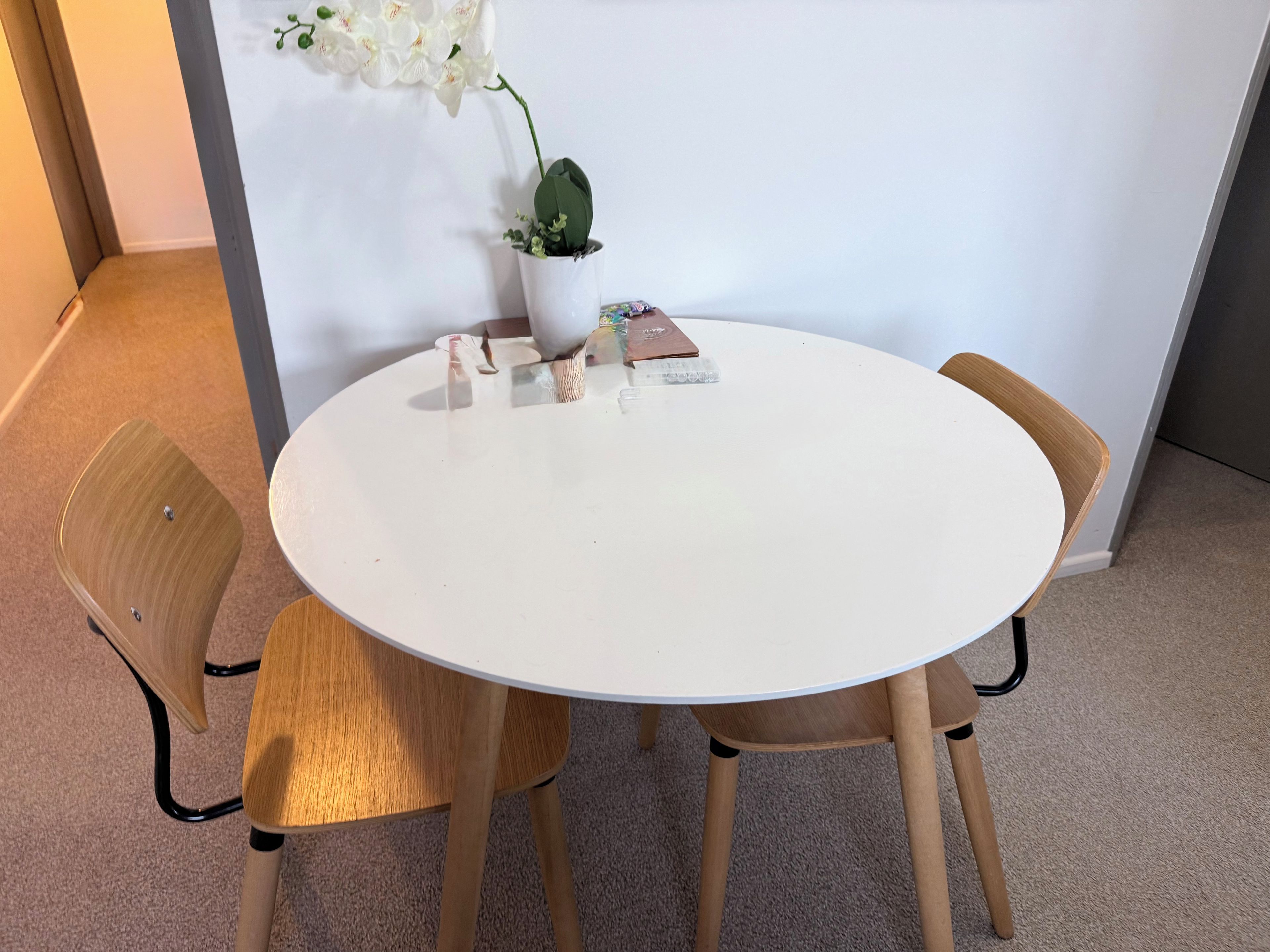 A round white table with four wooden chairs, a potted plant, and some items on the table.