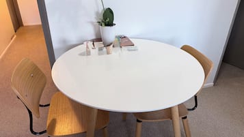 A round white table with four wooden chairs, a potted plant, and some items on the table.