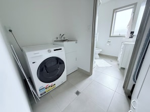 A laundry room with a Samsung washing machine, a sink, and a window.