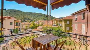Un balcon avec une table et des chaises, donnant sur un quartier résidentiel avec des maisons et une colline en arrière-plan.