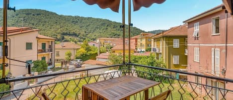 A balcony with a table and chairs, overlooking a residential area with houses and a hill in the background.