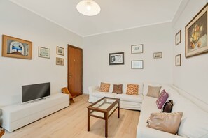 A living room with a flat-screen TV, a white sofa, a glass-top coffee table, and a wooden door. - [CasettaDellePunte]Road to lerici-Air conditioning (Romito Magra)