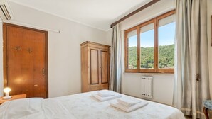 Ett hotellrum med en säng, en garderob i trä, ett element och ett fönster med utsikt över grönområden.