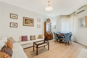 A living room with a sofa, coffee table, dining table with chairs, and a grandfather clock.