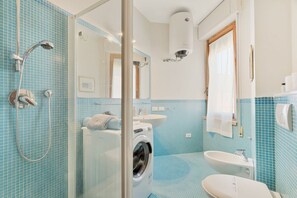 Et badeværelse med glasbrusekabine, vaskemaskine, vask og toilet.