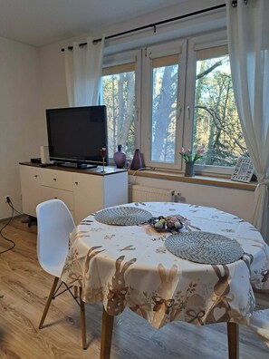 Ein Zimmer mit einem Esstisch für zwei Personen, einem Fernseher auf einer Kommode und einem Fenster mit Vorhängen.