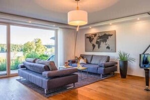 A modern living room with a sofa set, a coffee table, and a large window offering a view of greenery.