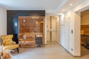A modern interior with a glass-enclosed sauna, a wooden bench, and a seating area with a sofa and cushions.