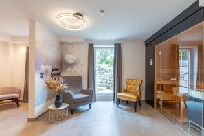 Ein modernes Wohnzimmer mit einem grauen Sofa, einem goldenen Sessel und einer dekorativen Vase mit Trockenpflanzen.