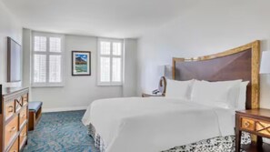 Een hotelkamer met een groot bed, een dressoir, een bureau en een raam met jaloezieën.