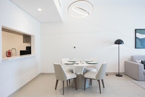 A modern dining area with a round table, white chairs, and a pendant light. - Bloomfields 1BR in Vantage 2- YGC (Abu Dhabi)