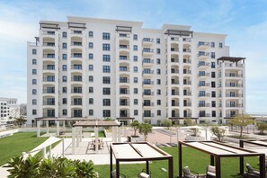 A multi-story hotel with balconies, outdoor seating areas, and a well-maintained lawn. - Bloomfields 1BR in Vantage 2- YGC (Abu Dhabi)