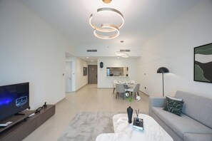 A modern living room with a flat-screen TV, a coffee table, and a sofa. There is a dining area with a table and chairs in the background. - Bloomfields 1BR in Vantage 2- YGC (Abu Dhabi)