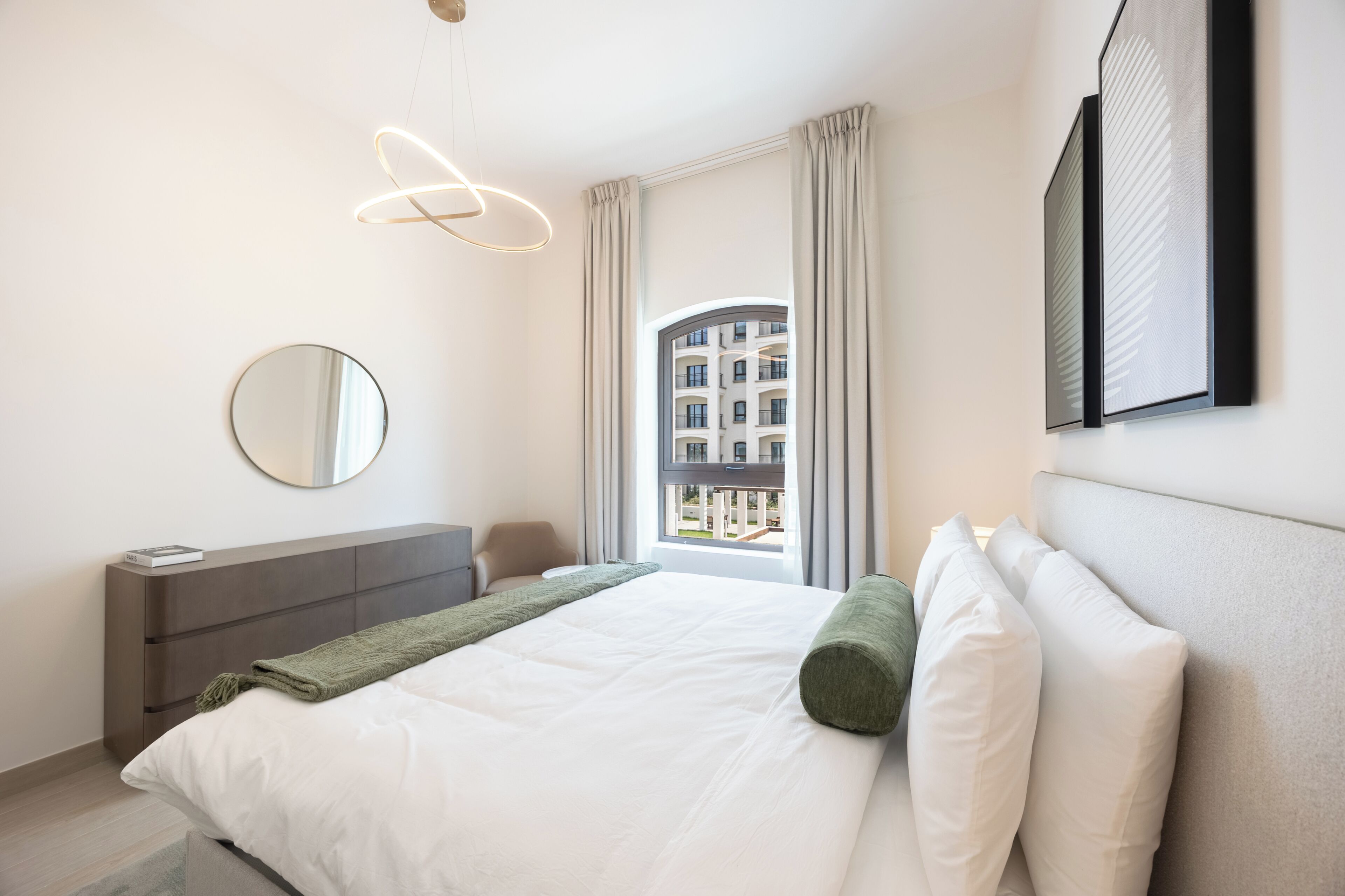 Quarto de hotel moderno com cama, mesa de cabeceira, espelho e vista para um edifício pela janela.