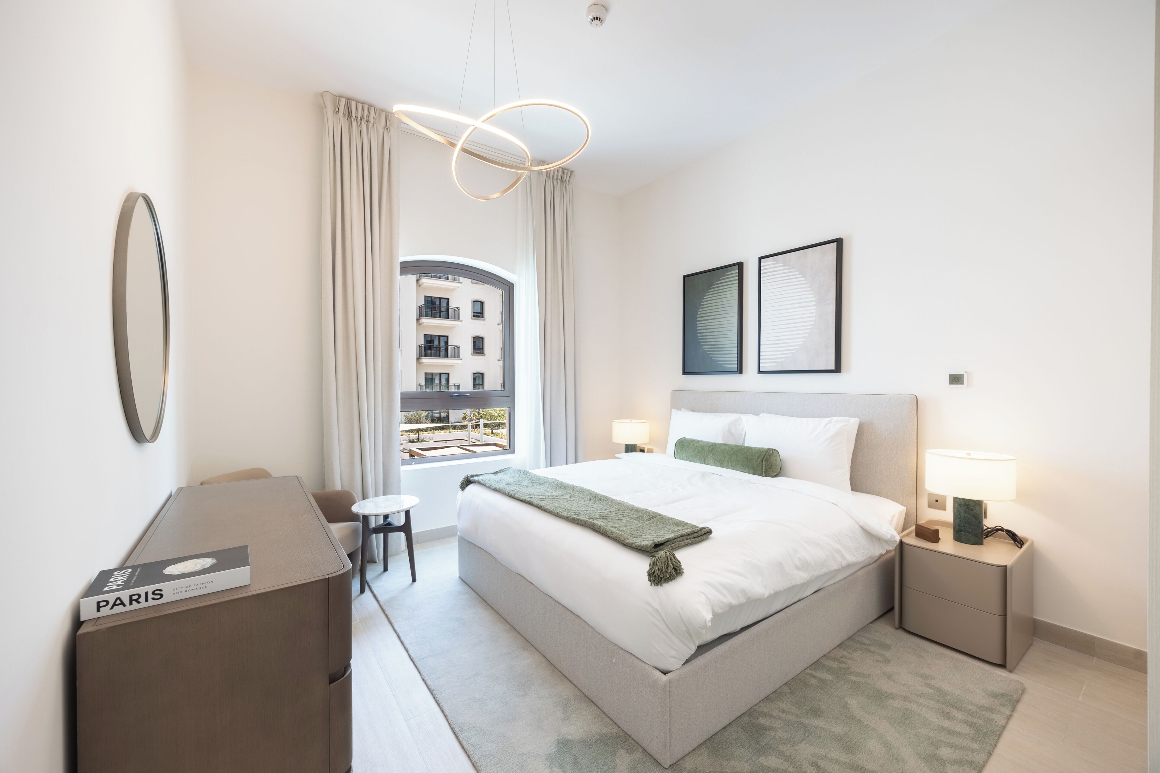 A modern hotel room with a large bed, bedside tables, a desk, and a view of the outside.