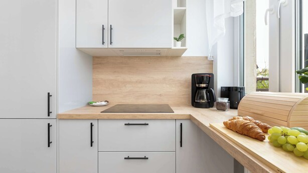 Ett modernt kök med vita skåp, en träbänkskiva, en kaffebryggare och ett bröd.