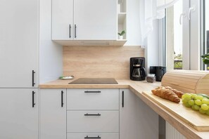 A modern kitchen with white cabinets, a wooden countertop, a coffee maker, and a loaf of bread. - Spacious Apartment with a Large Balcony | 3 Bedrooms (Gdańsk)