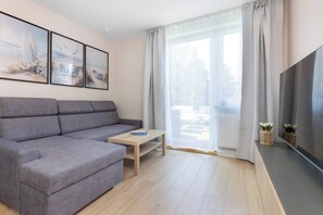 Uma sala de estar moderna com um sofá seccional cinza, uma mesa de centro de madeira e uma televisão de tela plana sobre um suporte.