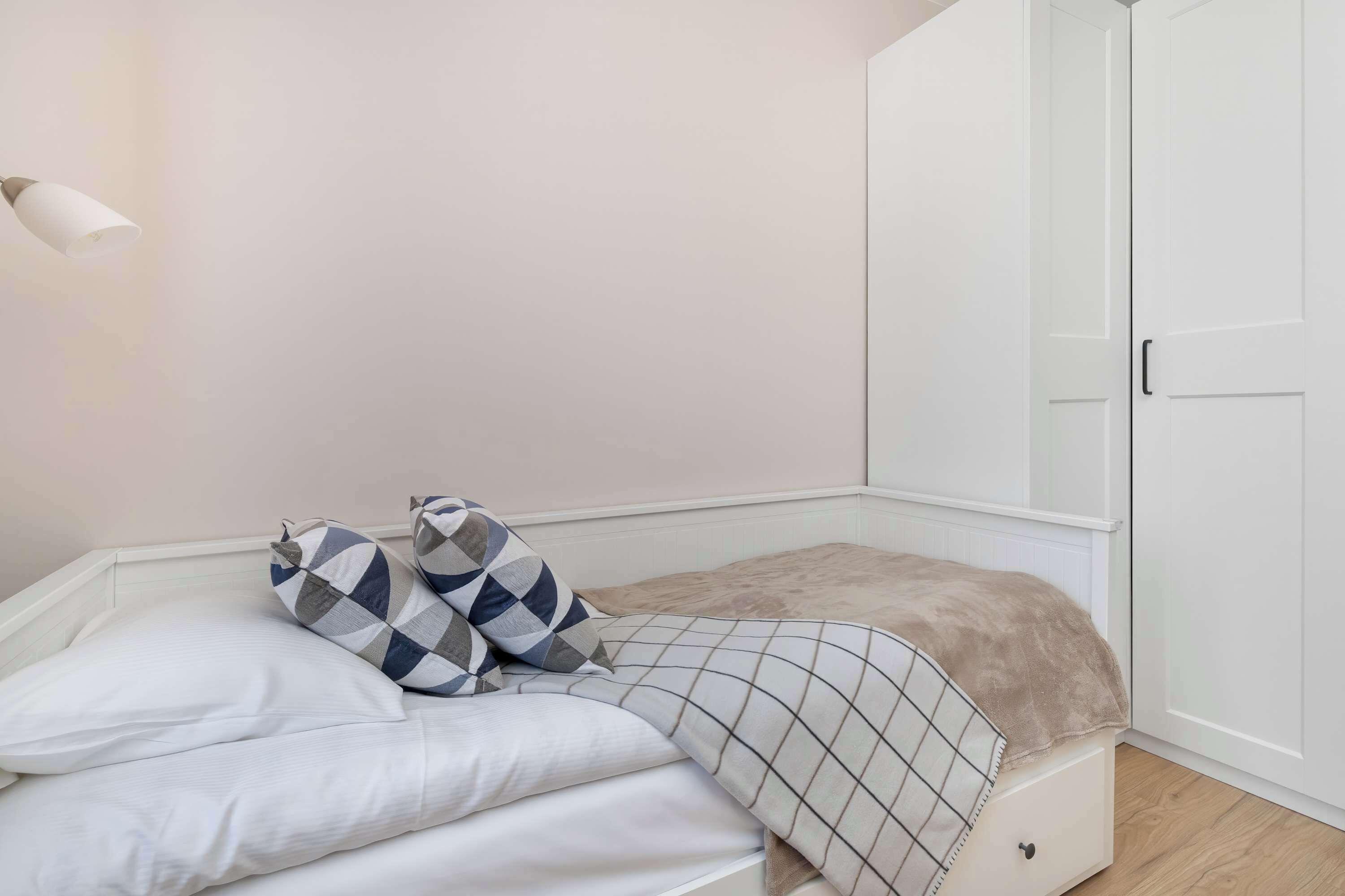 Een slaapkamer met een bed, nachtkastje, kledingkast en een wandlamp.