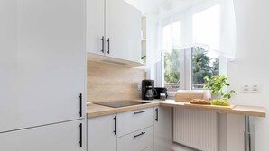 Ett modernt kök med vita skåp, en träbänkskiva, en kaffebryggare och ett fönster med utsikt över grönområden.