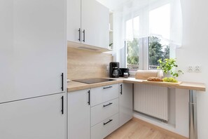 Eine moderne Küche mit weißen Schränken, einer Holzarbeitsplatte, einer Kaffeemaschine und einem Fenster mit Blick auf Grünflächen.