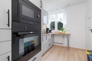 Cozinha moderna com eletrodomésticos embutidos, uma janela com cortinas leves e vista para o verde lá fora.