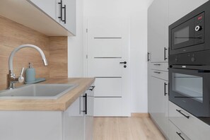A modern kitchen with a built-in oven, a sink with a faucet, and wooden cabinetry. - Spacious Apartment with a Large Balcony | 3 Bedrooms (Gdańsk)