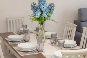 A dining table set with white plates, clear glassware, and a vase with blue flowers. - Spacious Apartment with a Large Balcony | 3 Bedrooms (Gdańsk)