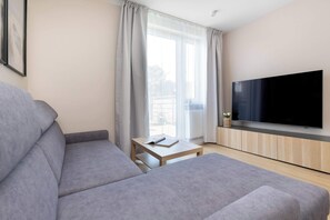 Ein modernes Wohnzimmer mit einem grauen Sofa, einem Flachbildfernseher und einem kleinen Tisch mit einem Buch.