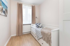 Um quarto com uma cama, um radiador, uma janela com cortinas e uma parede com um quadro.