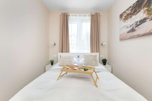 Ein Hotelzimmer mit einem Bett, einem Nachttisch, einem Fenster mit Vorhängen, einer Wandlampe und einem Gemälde.