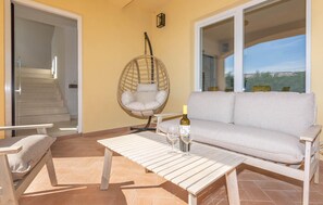 Un balcón con sofá, una silla colgante, una mesa y una botella de vino.
