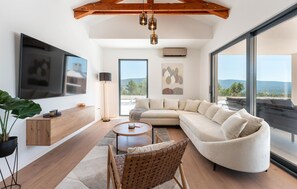 A modern living room with a sectional sofa, a round coffee table, a floor lamp, and a flat-screen TV mounted on the wall. - Villa Olive Tree Pridraga (Pridraga)