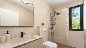 Et moderne badeværelse med et stort spejl, en vask med sort armatur, toilet og en bruseniche med glasvægge.