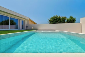 Ein rechteckiger Swimmingpool mit klarem, blauem Wasser, umgeben von einer weißen Mauer und einer Rasenfläche.