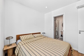 A bedroom with a bed, bedside tables, a lamp, and a door leading to a bathroom. - Casa Set - Private Pool Villa - 5 min to the Beach (A dos Cunhados)