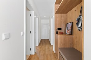 Ein Flur mit Holzboden, weißen Wänden und einer Bank mit Bilderrahmen und einer Flasche darauf.
