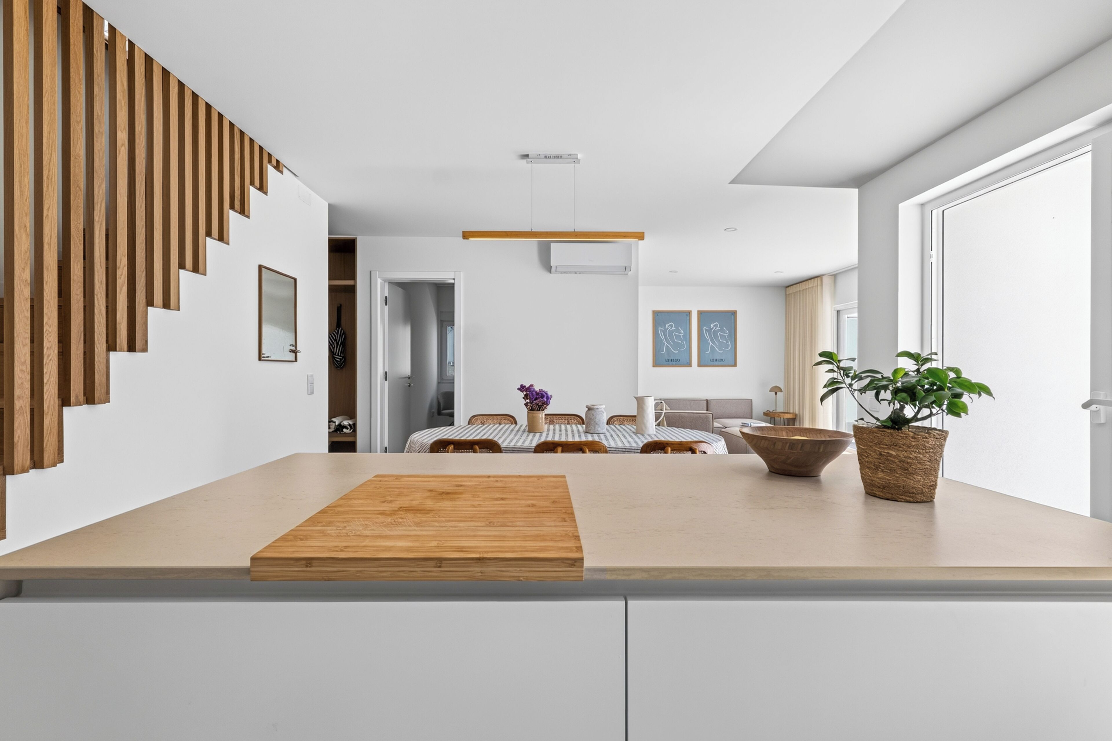Een moderne keuken met een houten aanrecht, een eethoek met een geribbelde tafelkleed en een trap met houten latten.
