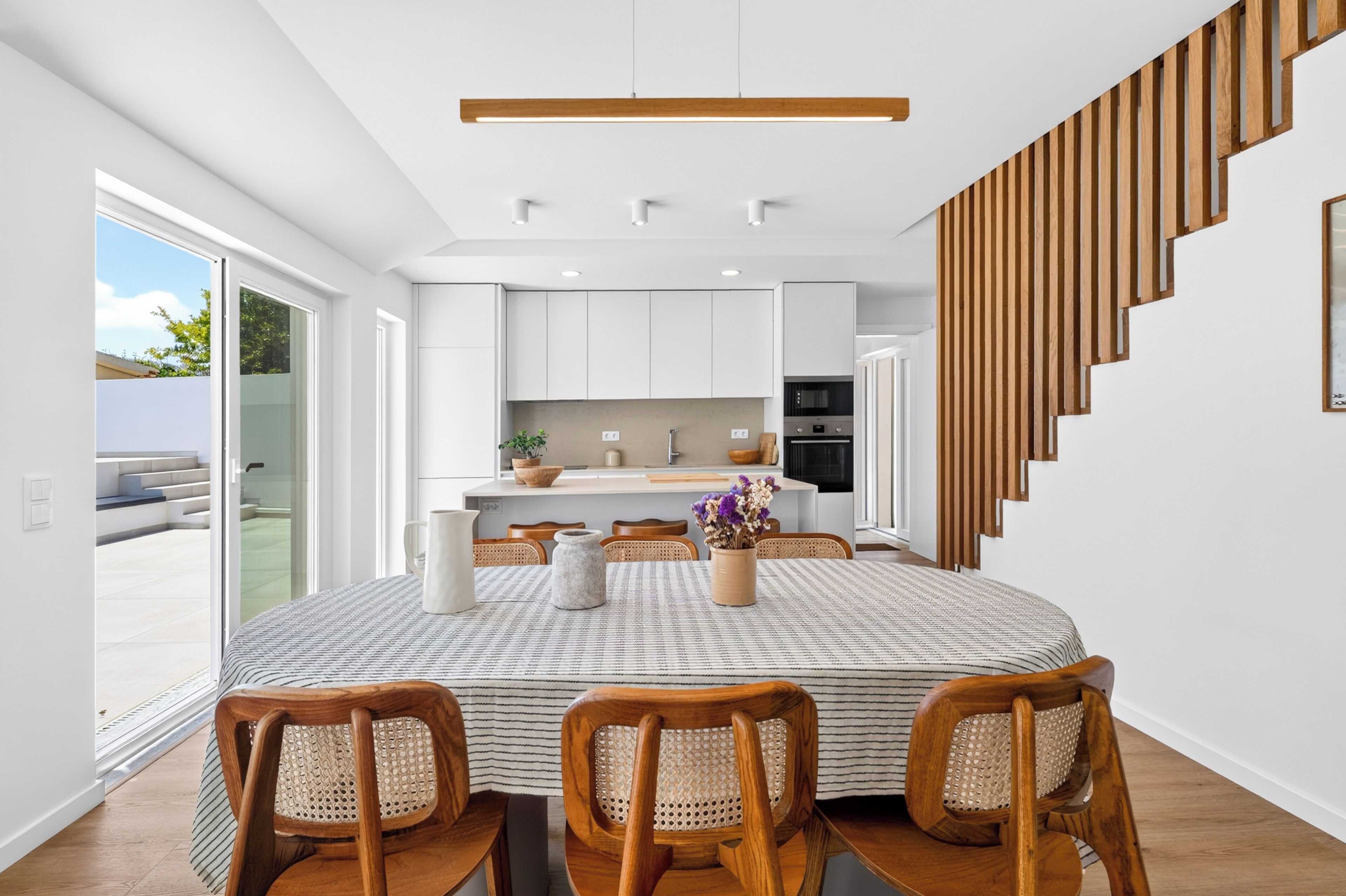 A modern kitchen with white cabinets, a central island, and a dining area with a round table and wooden chairs.