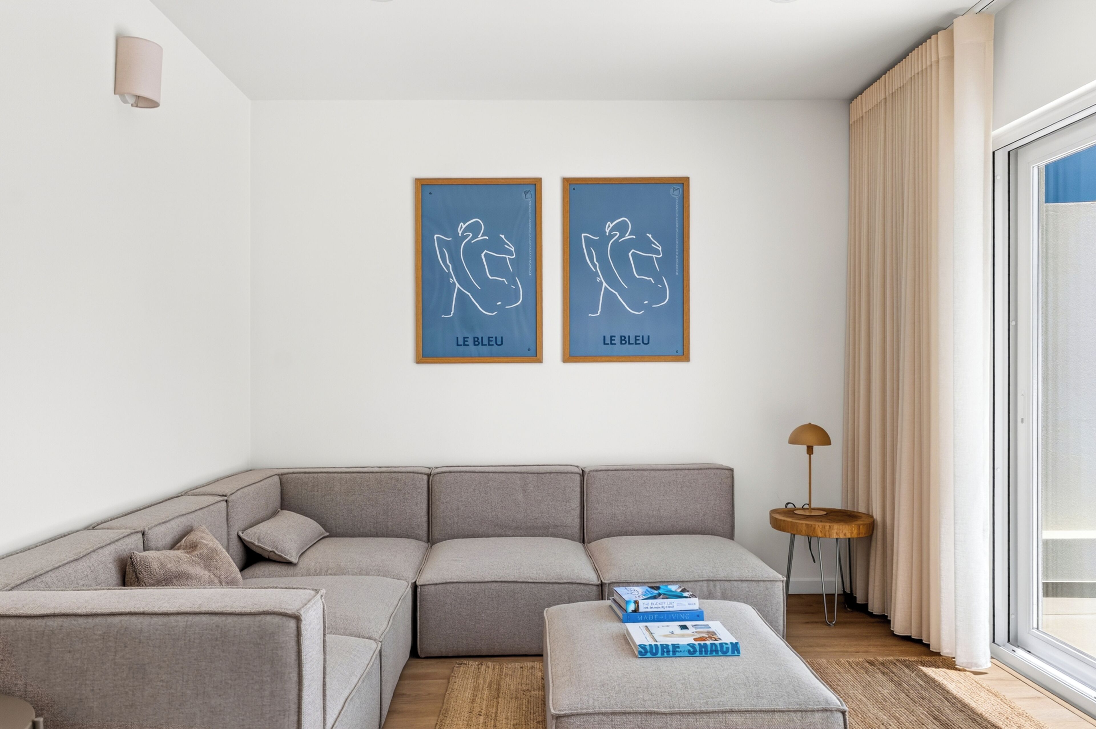 Una sala de estar moderna con un sofá seccional gris, una pequeña mesa redonda de madera y dos obras de arte enmarcadas en la pared.