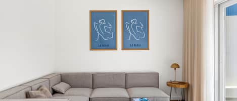 Una sala de estar moderna con un sofá seccional gris, una pequeña mesa redonda de madera y dos obras de arte enmarcadas en la pared.