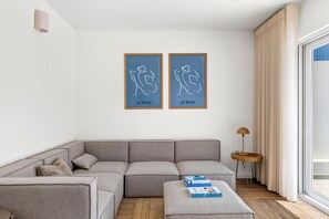 A modern living room with a grey sectional sofa, a small round wooden side table, and two framed artworks on the wall. - Casa Set - Private Pool Villa - 5 min to the Beach (A dos Cunhados)