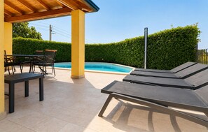 Ein überdachter Außenbereich mit Pool, Liegestühlen und einem Tisch mit Stühlen.