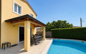 Ein gelbes Gebäude mit überdachter Terrasse, Schwimmbad und Hecke.